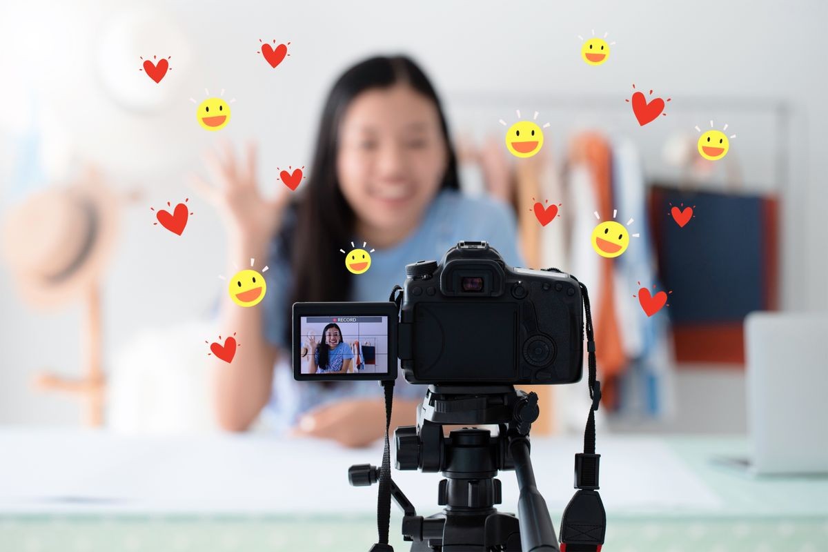 Beautiful asian woman blogger is talking in front of the camera to recording vlog video live streaming at home with heart and smile face icon.Business online influencer on social media concept.